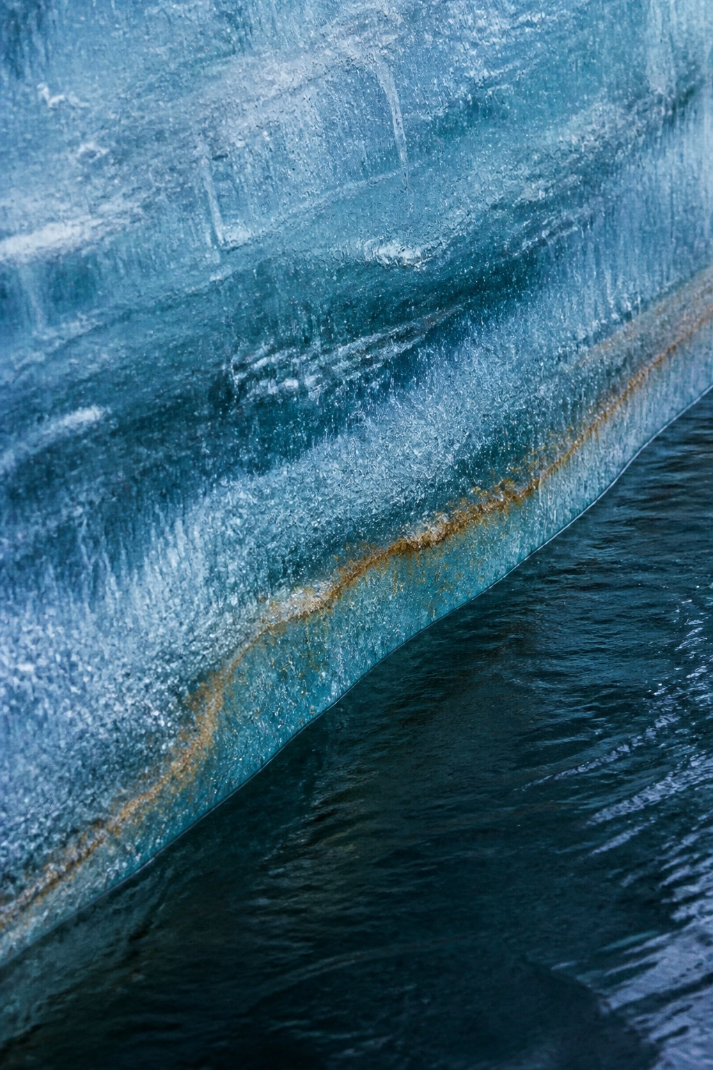 Blue glacier ice with a mineral seam above dark water